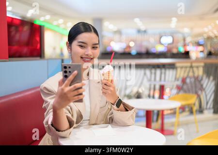 Portrait horizontal moyen d'une jeune femme d'affaires thaïlandaise d'Asie du Sud-est originaire de la région d'Isan souriant chaleureusement tout en tenant son smartphone dehors Banque D'Images
