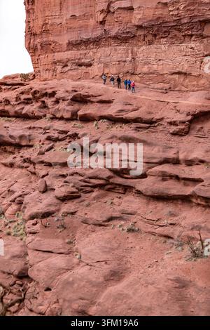 Un groupe de randonneurs emprunte un sentier étroit le long d'une falaise imposante en grès rouge des Fisher Towers près de Moab, Utah, États-Unis, par une journée nuageuse Banque D'Images