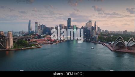 Vue panoramique du paysage urbain de Sydney au coucher du soleil avec les monuments emblématiques – l'Opéra et le pont du Harbour, baignés dans la lumière douce du crépuscule avec les gratte-ciel de la ville Banque D'Images