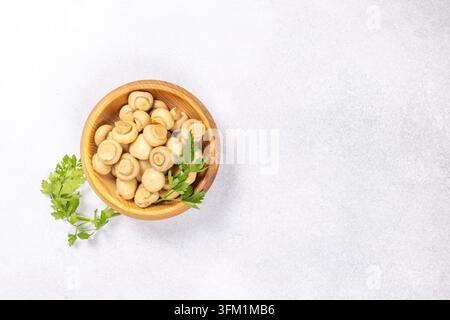 Champignons bien entretenus dans un bol en bois rustique, garnis de persil frais, posés sur un fond de pierre gris clair, invitant à une entrée saine ou s Banque D'Images