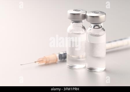 Vialettes contenant un vaccin et seringue sur une table blanche, gros plan Banque D'Images
