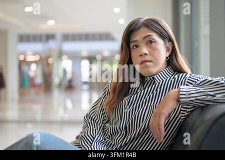 Thai Isan femme d'affaires transgenre dans les années 40 assis dans le hall du bureau regardant la caméra. Portrait horizontal moyen d'un Sud-est non binaire mature Banque D'Images
