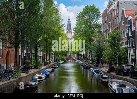 Bateaux amarrés et maisons de canal bordées d'arbres le long de la Groenburgwal, avec la tour de la Zuiderkerk en arrière-plan, Amsterdam, Pays-Bas. Banque D'Images