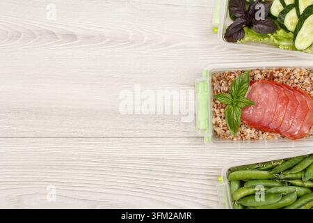 Récipient en plastique avec des pois verts frais, du porridge de sarrasin bouilli et des tranches de viande, concombre et laitue sur un fond gris. Vue de dessus avec c Banque D'Images