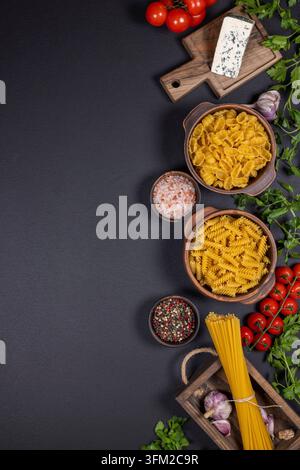 Divers types de pâtes non cuites avec tomates cerises mûres. Persil frais. Ail. Fromage bleu. Et assaisonnement différent dans de petits bols. Tous disposés sur un Banque D'Images