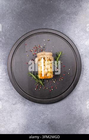 Champignons bien entretenus dans un bocal en verre. Collés avec une ficelle rustique et une patte. Assis sur une planche de bois sombre entourée de plants de romarin frais et de pep mélangé Banque D'Images