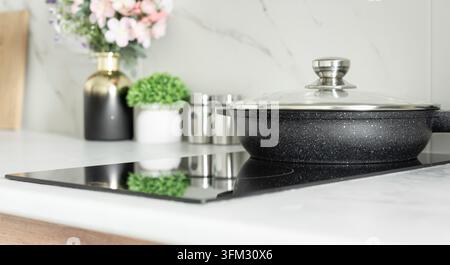 Poêle antiadhésive avec couvercle en verre sur plaque à induction dans un intérieur de cuisine moderne et lumineux Banque D'Images