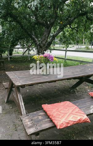 Bouquet de fleurs sauvages dans un vase en verre sur une table de pique-nique en bois dans le jardin Banque D'Images