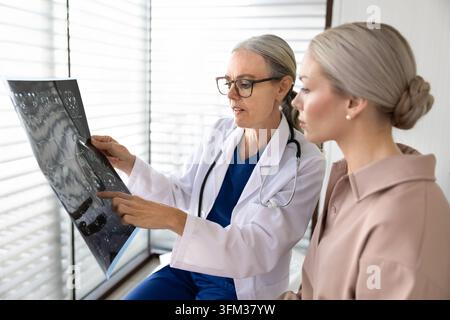 Docteur tenant une radiographie, expliquant le résultat du scanner à une patiente Banque D'Images