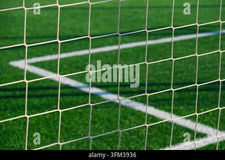 Filet de but de football blanc vu de près contre un gazon artificiel d'un vert vif avec des marquages de champ s'entrecroisant et un motif géométrique de mailles dans un espace sportif extérieur Banque D'Images