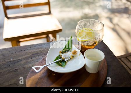 Une assiette de dessert avec une pâtisserie à la crème, une boisson au citron, une tasse de café et une chaise en bois sur une table d'extérieur rustique Banque D'Images