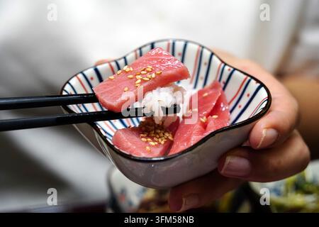 Main tenant un bol en céramique avec une bouchée de sushi au thon maguro et des baguettes Banque D'Images