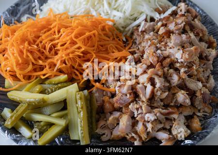 Ingrédients pour un shawarma ou un kebab fait maison sur une assiette : viande de poulet hachée, chou blanc râpé, carottes fraîches râpées et cornichons tranchés prêts fo Banque D'Images