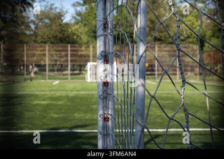 Filet de but de football au premier plan avec un terrain de football flou, des lignes et un autre but au loin, prêt à jouer Banque D'Images