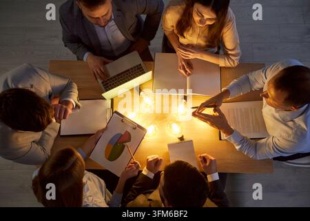 Vue aérienne d'une équipe d'affaires autour d'une table avec des ampoules, discutant des idées et planifiant une stratégie créative. Banque D'Images