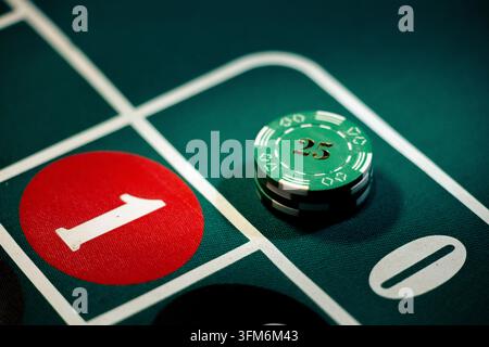 La table de roulette verte du casino présente des jetons empilés placés sur le zéro. Des jetons colorés recouvrent la case verte pendant le jeu actif. Banque D'Images