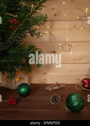 Nature morte de Noël avec des branches de feuillage persistant, des ornements verts et rouges, des pommes de pin et des guirlandes lumineuses chaudes sur un fond en bois Banque D'Images