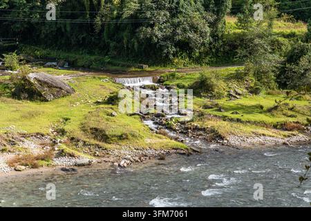 Un petit ruisseau rocheux avec un petit barrage s’écoule dans une rivière de montagne à travers des champs herbeux au Népal. Banque D'Images