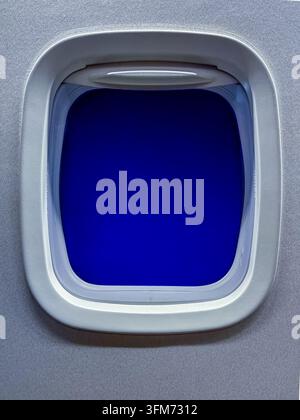 Close-up d'une fenêtre d'avion passager encadrant une vue matinale d'un bleu profond et sans relief pendant un voyage aérien. Banque D'Images