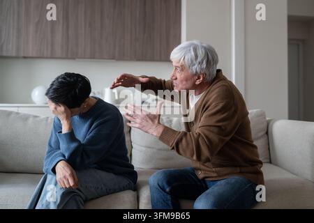 Homme âgé agressif et furieux criant et gesticulant face à sa femme stressée en pleurs lors d'un conflit familial. Banque D'Images