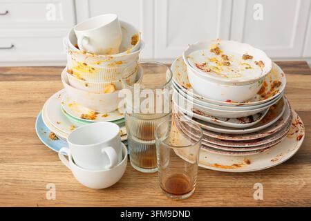 Tâches ménagères et épuisement domestique, pile de vaisselle sale et assiettes tachées sur une table de cuisine en bois après un repas avec des restes de nourriture et des taches Banque D'Images