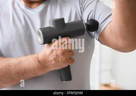 Récupération musculaire et thérapie physique, homme senior utilisant une pistolet de massage pour soulager les douleurs au bras et réhabiliter les blessures sportives dans un cadre de santé à domicile Banque D'Images