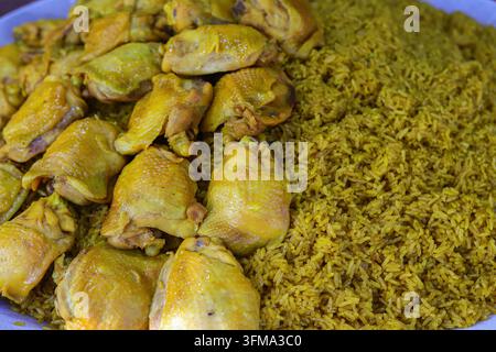 Khao mok gai thaïlandais avec du riz jaune épicé au curcuma et des cuisses de poulet, cuits ensemble et disposés côte à côte sur un grand plateau de service. Banque D'Images