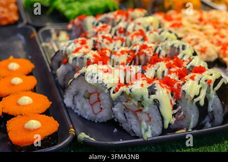 Rolles de sushi garnis de tobiko, sauce à la mayonnaise crémeuse et nigiri d’imitation de crabe sur un plateau noir posé sur une pelouse artificielle. Banque D'Images