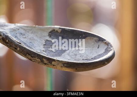 Vue macro détaillée d'une cuillère en bois rustique et patinée montrant des surfaces usées et un fond doux jaune étincelant Banque D'Images