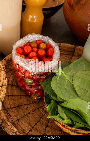 Tomates cerises rouges fraîchement cueillies dans un sac transparent et des feuilles d'épinards vert vif reposant dans un panier en osier, représentant une alimentation saine, orga Banque D'Images