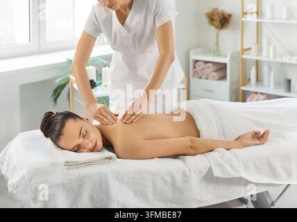 Belle femme profitant d'un massage du dos par un thérapeute professionnel, allongée sur un canapé les yeux fermés Banque D'Images