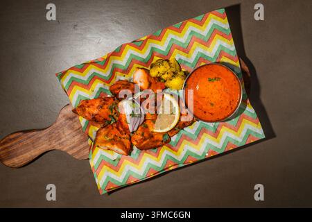 Poulet tandoori avec des quartiers de citron et une sauce de trempage sur une planche en bois, vue de dessus Banque D'Images