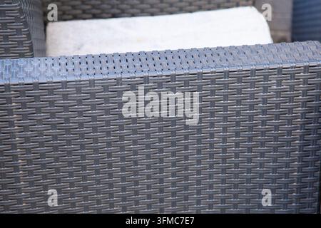 Vue rapprochée d'une chaise de patio tissée grise avec un coussin clair montrant la texture du rotin Banque D'Images