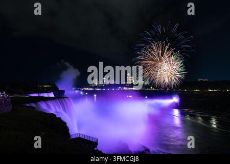 Feux d'artifice explosant au-dessus des chutes du Niagara illuminées en violet la nuit Banque D'Images