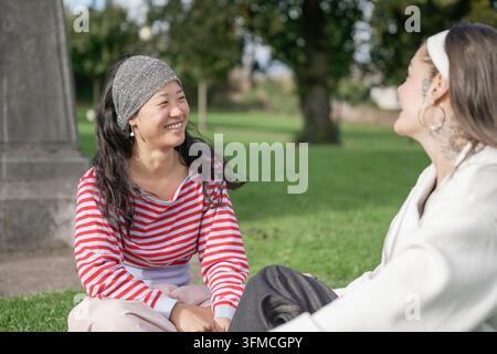 Amis assis sur l'herbe, riant et profitant d'une conversation Banque D'Images