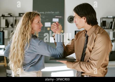 Femme et homme s'affrontant au bras de fer dans un bureau pour un concept de rivalité Banque D'Images