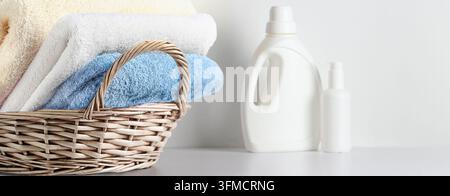 Panier en osier avec des serviettes jaunes crème et bleues pliées à côté du détergent Banque D'Images