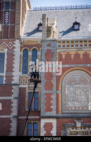 15 juillet 2024, Amsterdam, Pays-Bas : des ouvriers de maintenance utilisent une plateforme aérienne sur la façade en briques ornée du Rijksmuseum, en dessous d'une figure sculptée Banque D'Images