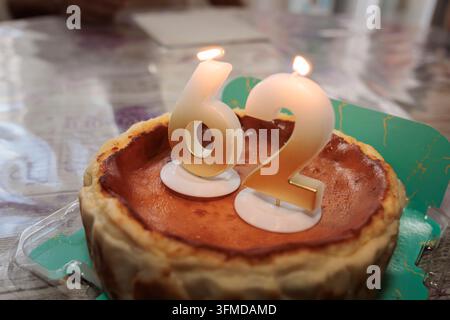 Cheesecake d'anniversaire avec bougies allumées affichant le nombre 62 Banque D'Images