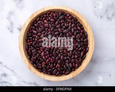 Haricots rouges dans un bol en bois sur une table en marbre, vue de dessus Banque D'Images