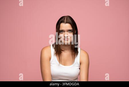 Jeune femme contrariée se sentant frustrée et confuse, arborant une expression triste sur le visage devant un fond rose Banque D'Images