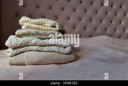 Pile soigneusement empilée de pulls pliés et sweat-shirt beige sur un lit rose confortable avec un fond élégant. Banque D'Images