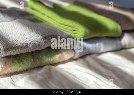 Range de pulls en laine tricotés colorés soigneusement pliés disposés sur un drap de lit dans la lumière douce du matin. Concept de sélection de garde-robe capsule, saisonnier Banque D'Images
