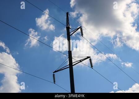 Les lignes électriques se dressent haut contre le ciel bleu rempli de nuages. La scène montre des poteaux et des fils électriques visibles dans une zone ouverte. Banque D'Images