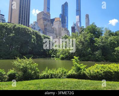 Lac de Central Park avec des arbres verts et des gratte-ciel de Manhattan sous un ciel bleu à New York City. Banque D'Images