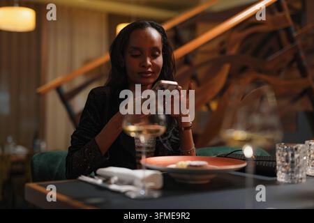 Femme prenant une photo d'un dessert délicieux avec son smartphone pendant un dîner dans un restaurant de luxe, prise de vue en gros plan. Banque D'Images