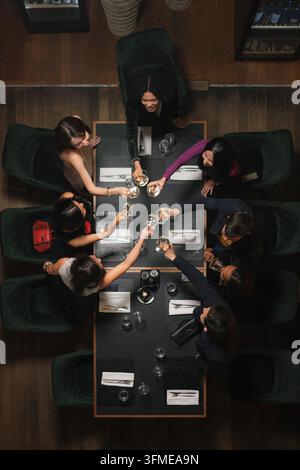 Groupe de personnes diversifiées, six amis passant un bon moment ensemble, profitant d'un dîner dans un restaurant moderne de luxe, vue de dessus. Banque D'Images