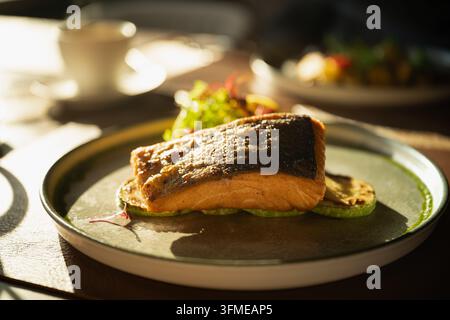 Filet de saumon grillé servi avec des courgettes et des légumes verts frais sur une assiette en céramique, avec une tasse de café en arrière-plan flou. Déjeuner au restaurant à wa Banque D'Images