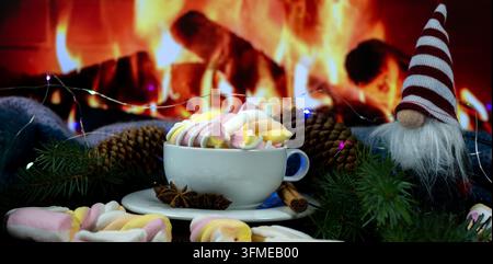 Fond de Noël et Nouvel An avec nain de jardin, tasse à guimauve, pommes de pin et cannelle près d'un feu de cheminée, décoration de fête Banque D'Images