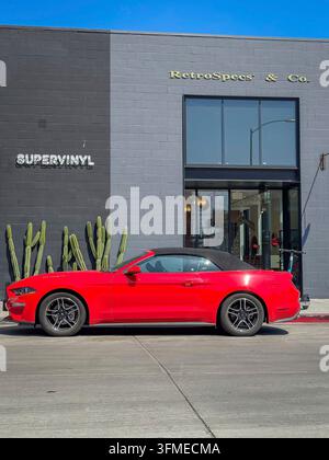 Hollywood, Los Angeles, Californie, États-Unis - 18 avril 2024 : Une voiture décapotable rouge est garée sur une rue ensoleillée. Le véhicule se distingue sur un fond stylé Banque D'Images